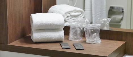 Una barra de madera con una toalla blanca doblada, dos sobres pequeños y tres botellas de vidrio transparente.
