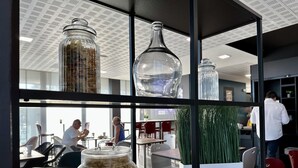 A modern office space with glass partitions, a variety of glass containers on shelves, and a dining area with tables and chairs. - Campanile Belfort Montbéliard - Gare La Jonxion (Meroux-Moval)