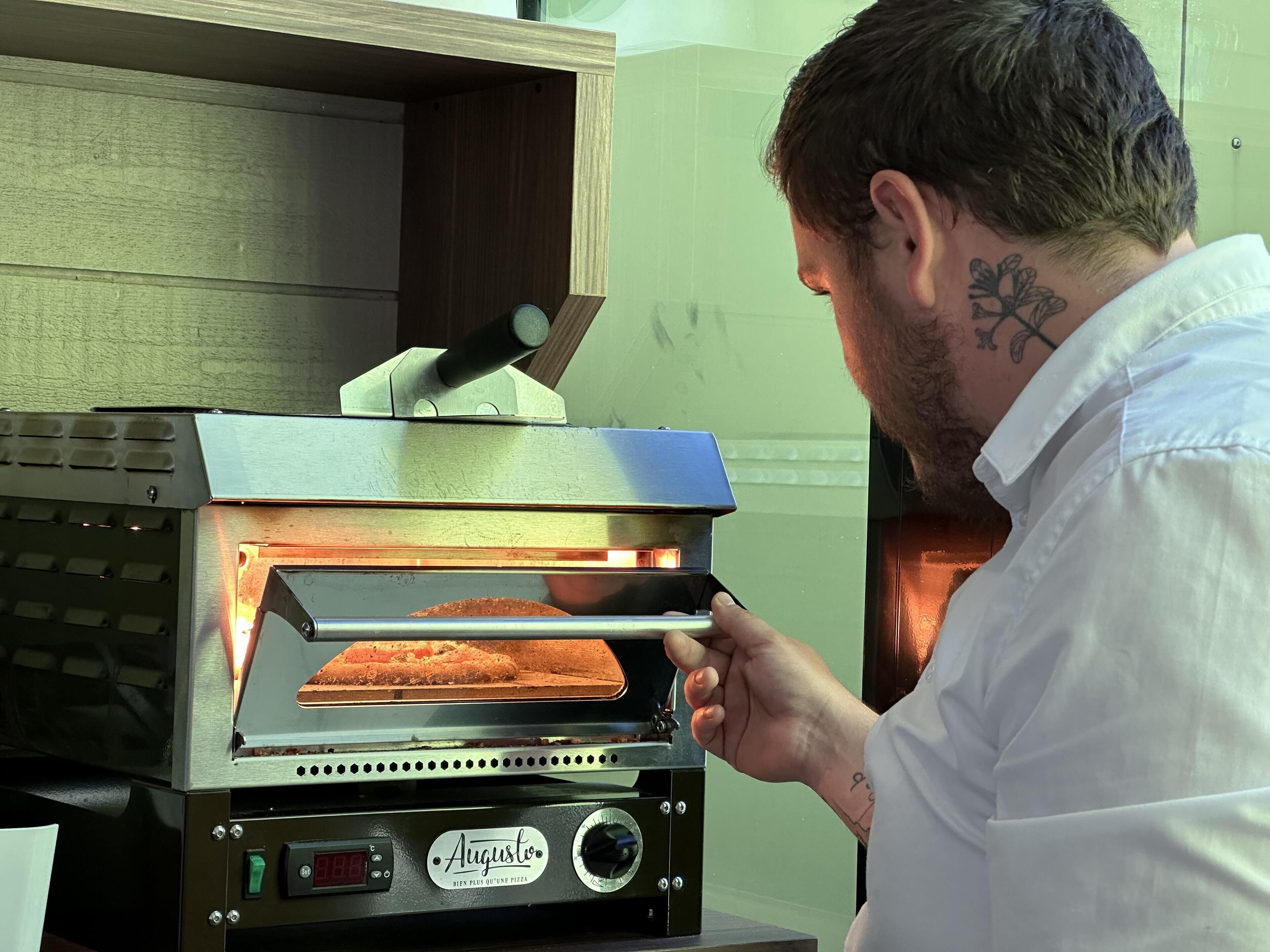 Eine Person bedient einen Pizzaofen mit digitaler Anzeige und Drehknopf.
