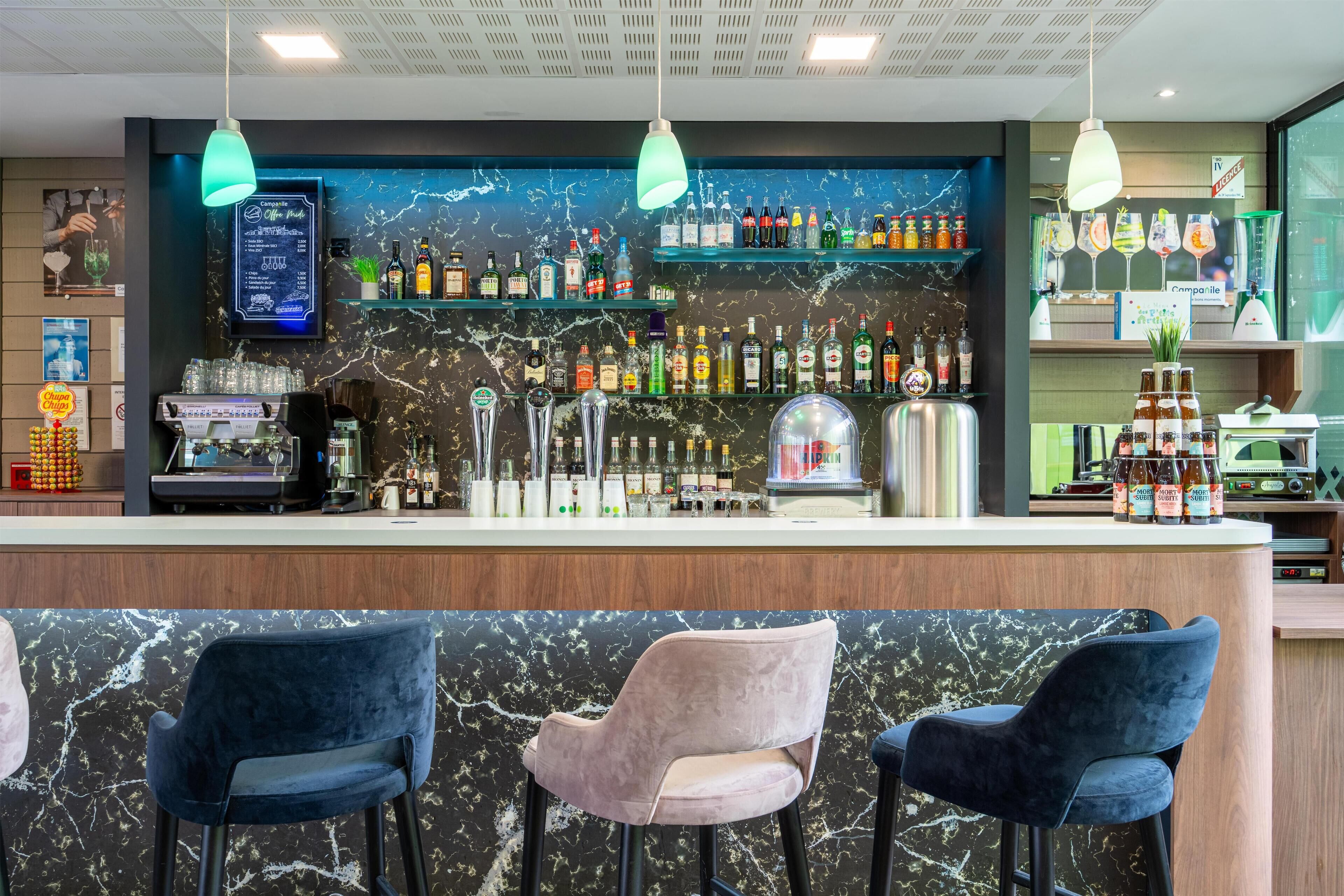 Una zona de bar con encimera de mármol, varias botellas de licor, un tablero de menú y taburetes de bar.