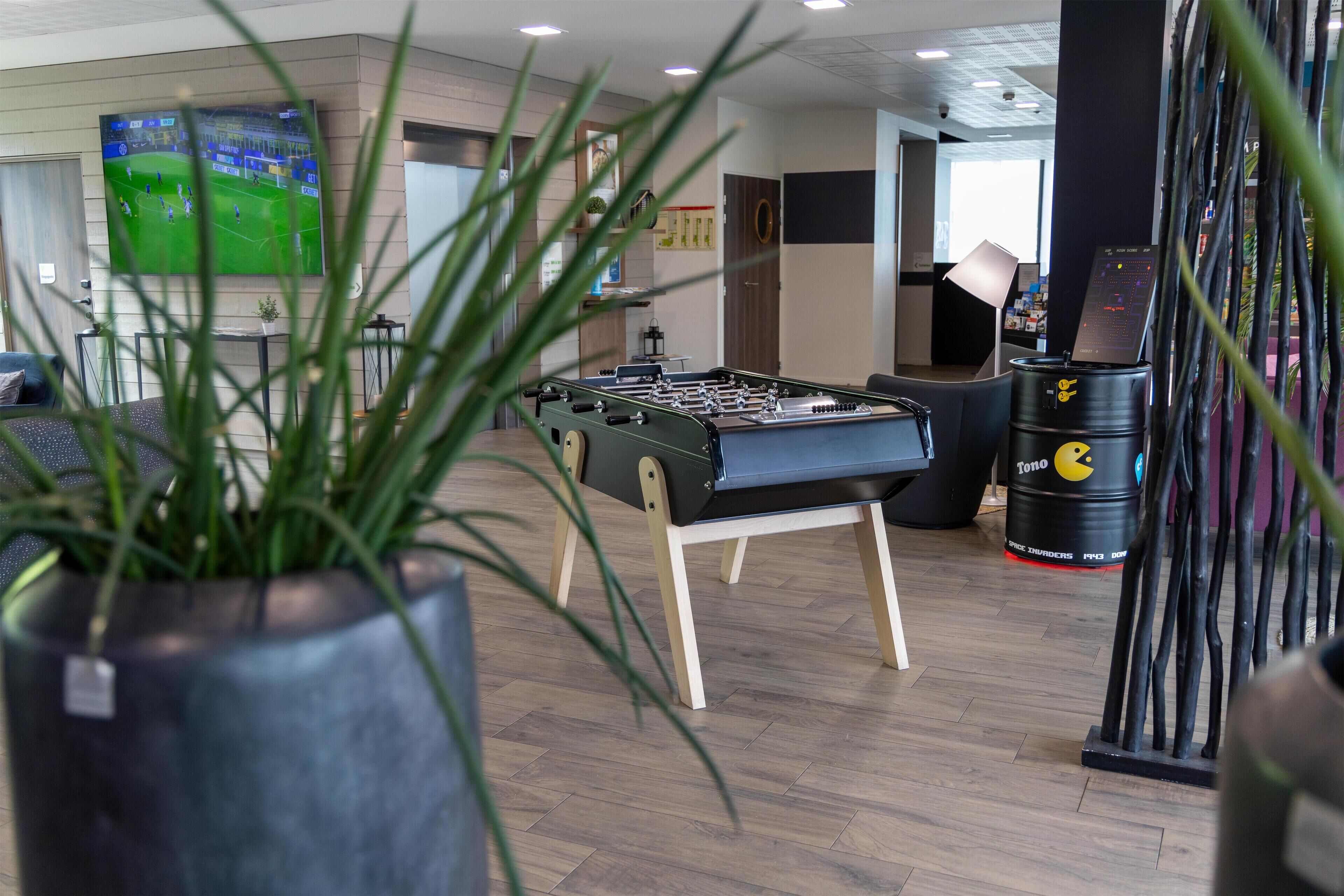 A room with a foosball table, a TV displaying a soccer game, and a Tono barrel.