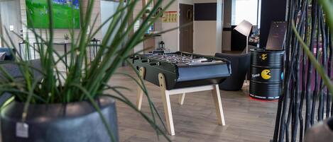 A room with a foosball table, a TV displaying a soccer game, and a Tono barrel.