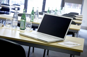 Een laptop op een bureau met een fles water, brillen en een pen.