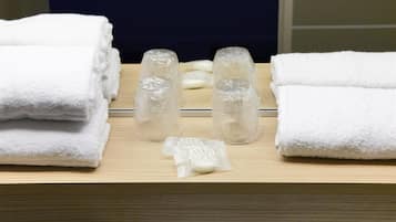 A bathroom with neatly stacked white towels, two glass bottles, and a bar of soap on a wooden surface.