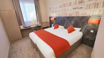 Ein Hotelzimmer mit einem großen Bett, einem Schreibtisch, einem Stuhl, einem Bücherregal und einem Fenster mit Vorhängen.