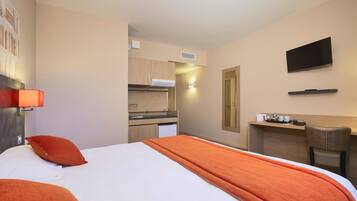 A hotel room with a bed, a desk, a television, and a kitchenette.