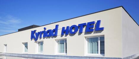 A modern hotel building with the name "Kyriad Hotel" prominently displayed on the facade.