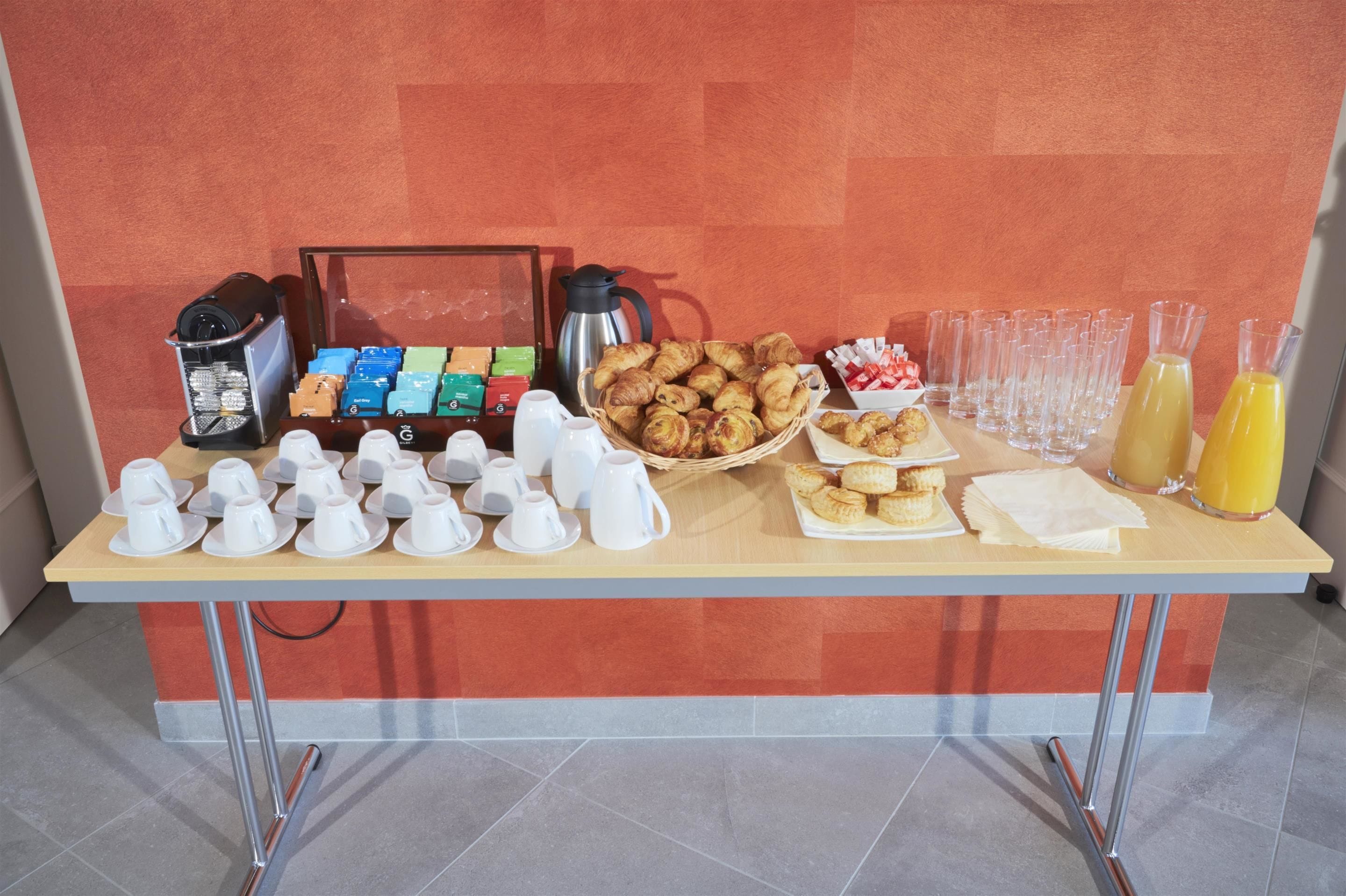 A breakfast buffet table with various food items, coffee machines, and glassware.