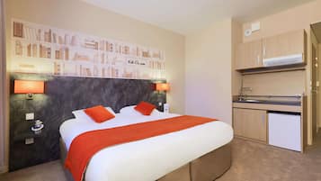 A hotel room with a bed, a small kitchenette, and a wall with a bookshelf.