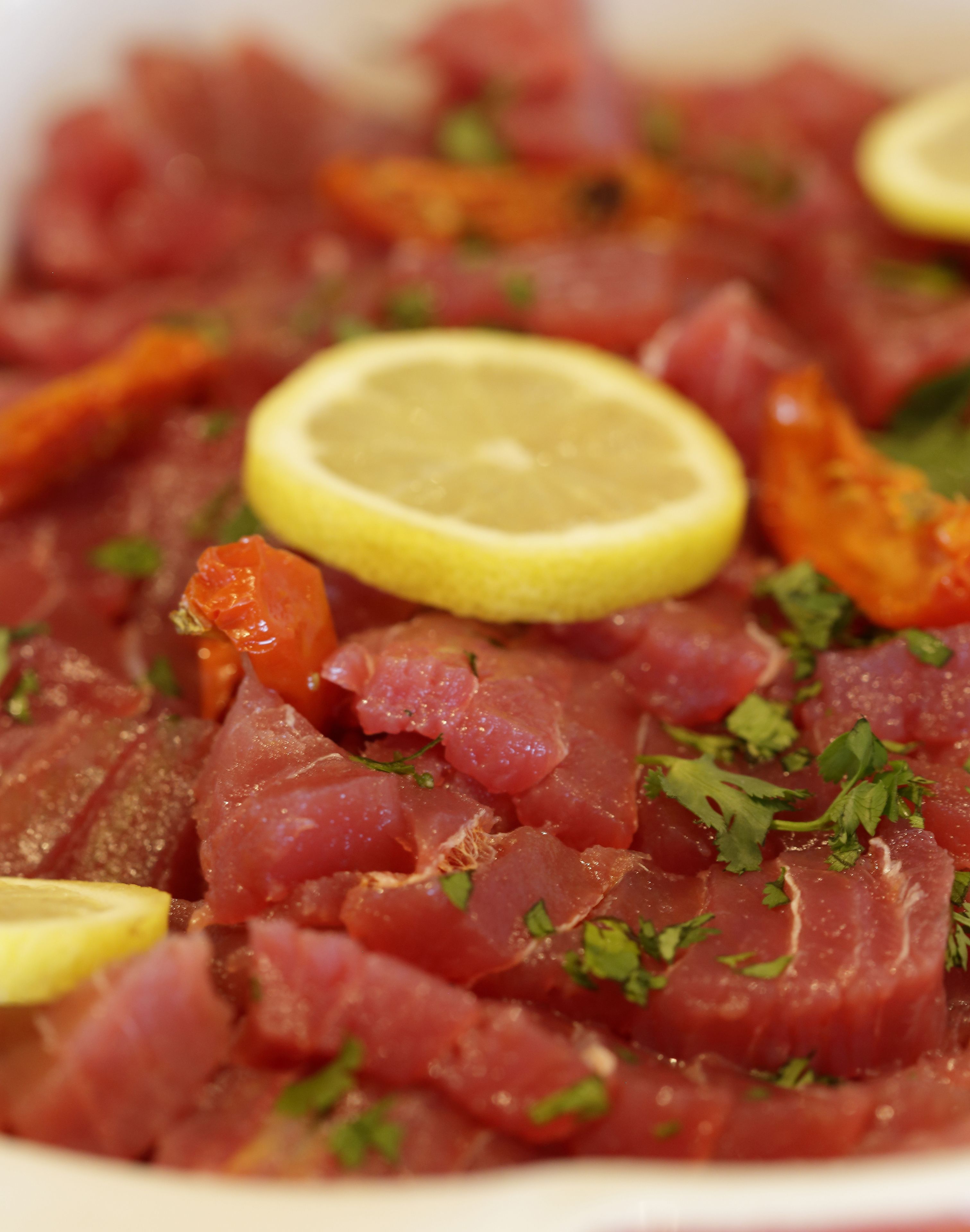 A close-up of a dish with raw meat, lemon slices, and herbs.