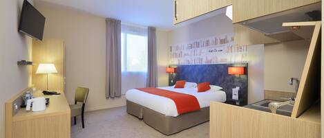 A hotel room with a bed, desk, chair, TV, and a small kitchenette.