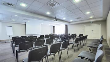 A conference room with rows of chairs, a projector, a whiteboard, and a door.