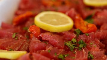 A close-up of a dish with raw fish, lemon slices, and herbs.