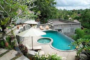 Piscina privada con hidromasaje, rodeada de escalones de piedra y abundante vegetación.