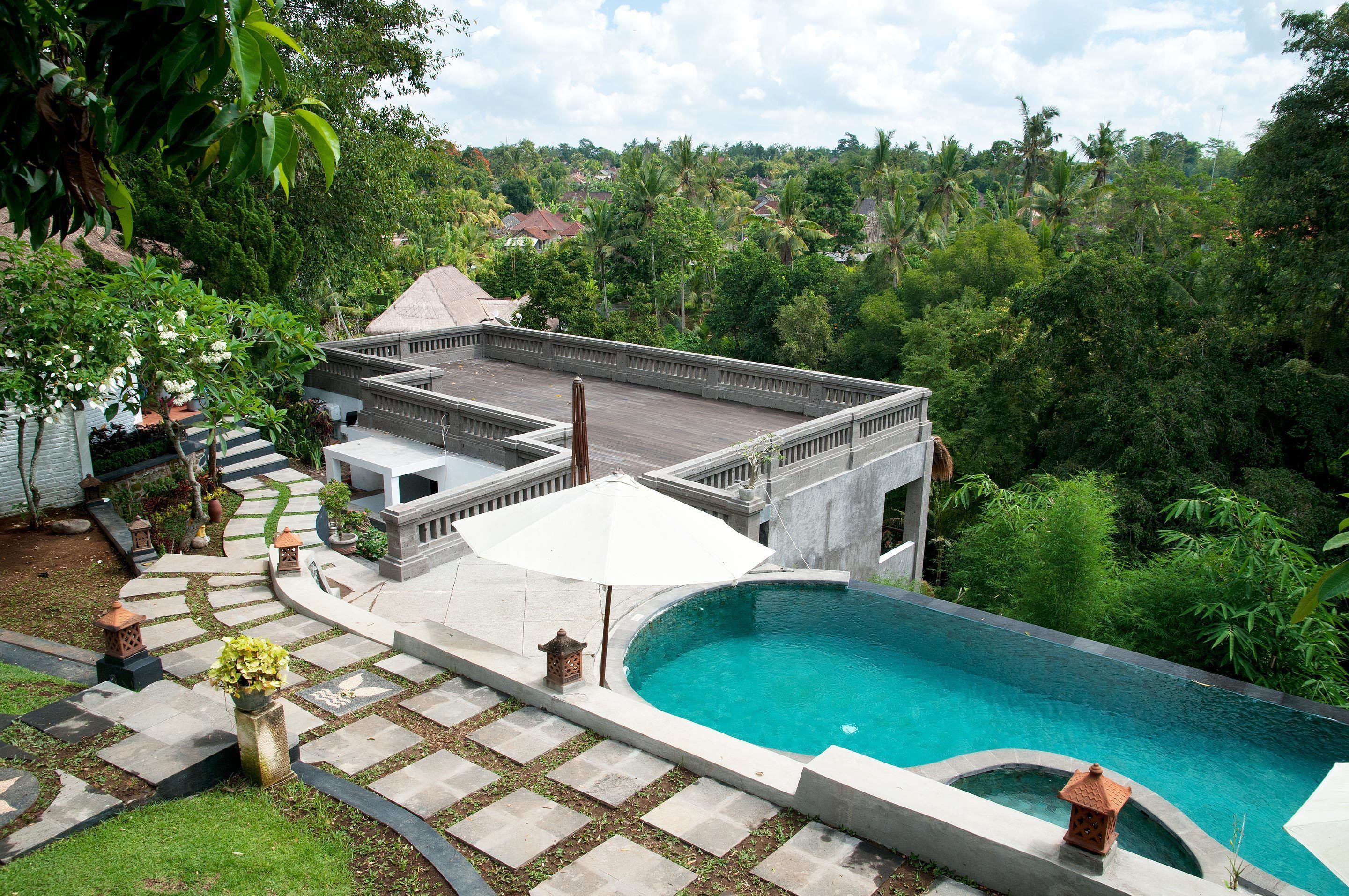 A rooftop pool area with a curved pool, stone pathways, and a small garden with a lantern.