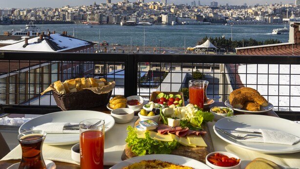 A table with a variety of food items and a view of a cityscape over water. - Sayeban Gold Hotel (Istanbul)
