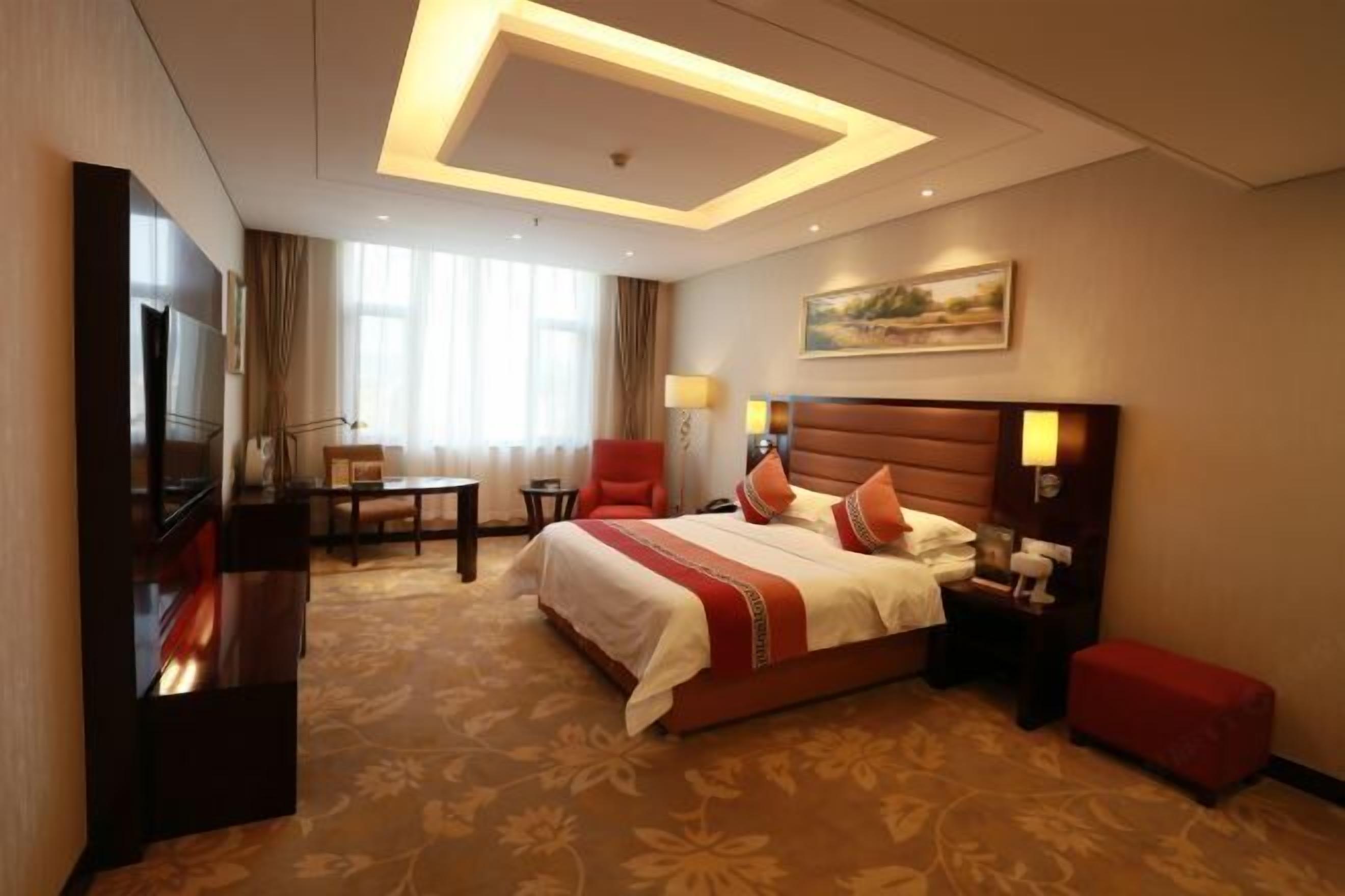 A hotel room with a large bed, a desk, a TV, and a painting on the wall.