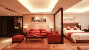 Una habitación de hotel moderna con una cama grande, un sofá rojo, una mesa de centro y un cuadro en la pared.