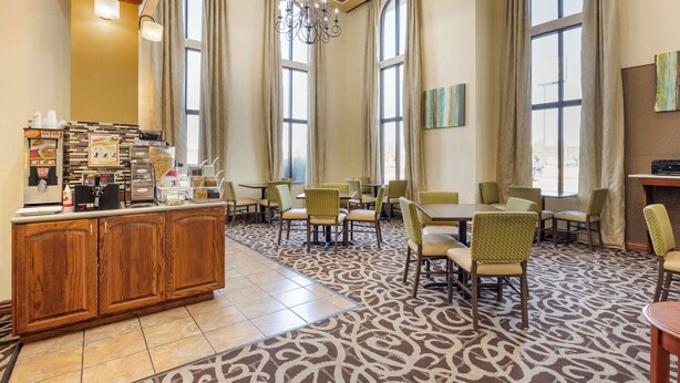 A hotel lobby with a central bar area, multiple dining tables and chairs, large windows, and a patterned carpet.