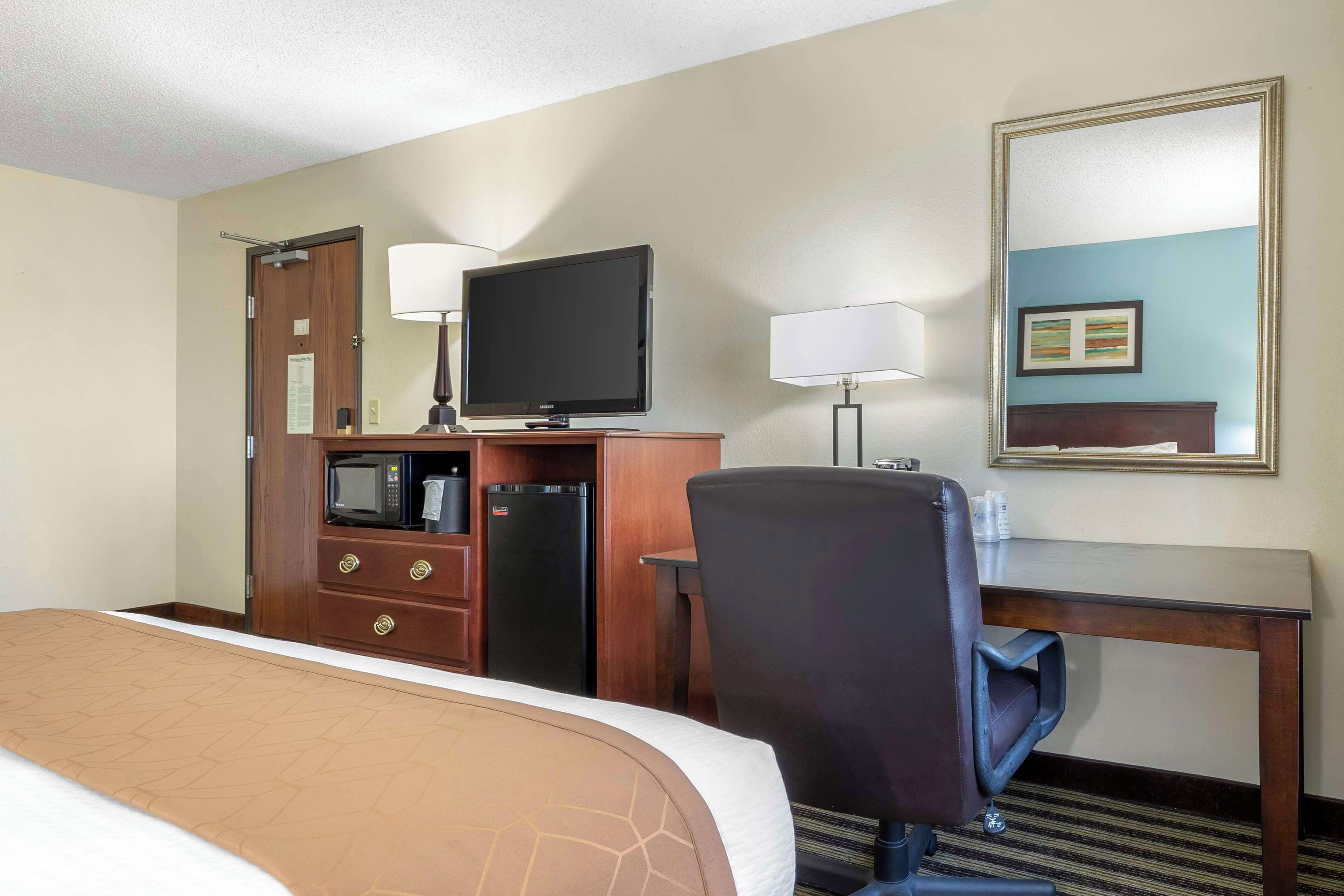 A hotel room with a bed, a desk with a computer, a television, a microwave, and a refrigerator.