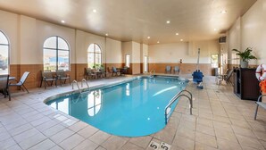 An indoor swimming pool with clear water, surrounded by lounge chairs and tables, and large windows providing natural light.