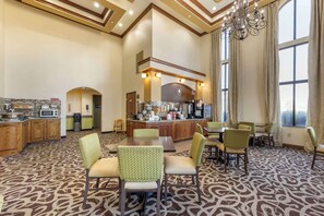 A hotel lobby with a central bar area, seating arrangements, and a kitchen in the background.