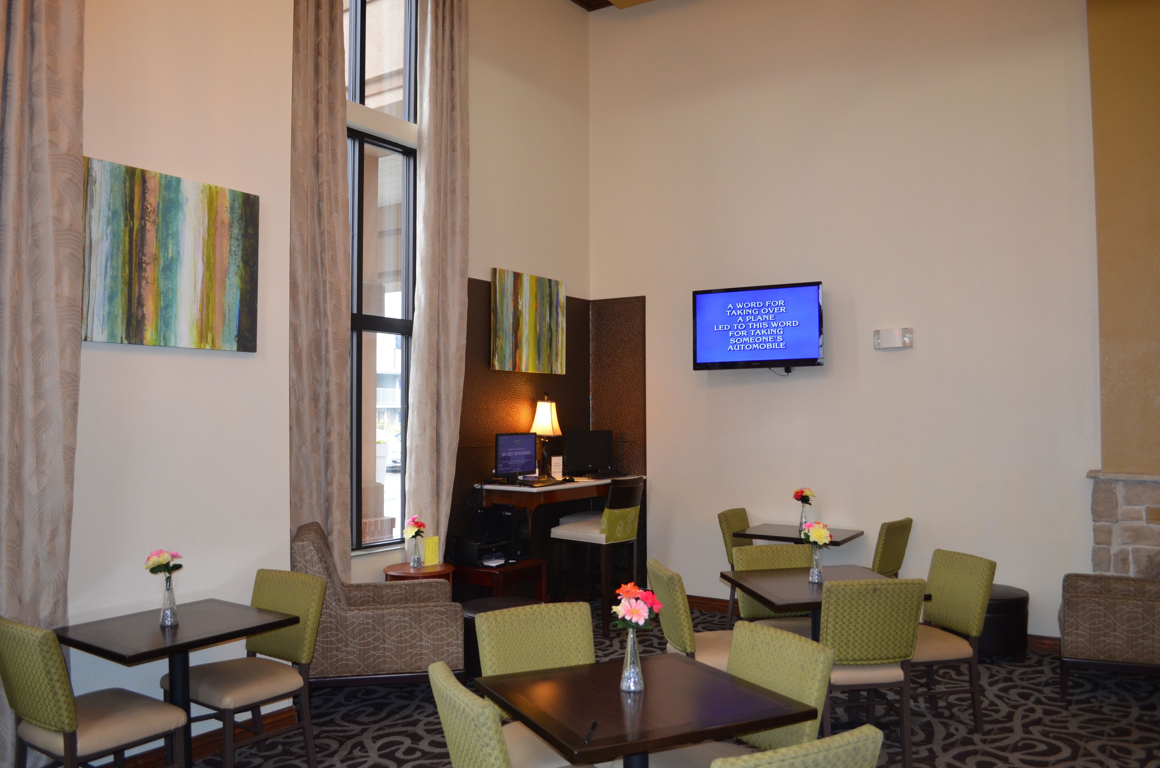 Habitación de hotel con escritorio, computadora, televisor y zona de estar con sillas y una mesa.