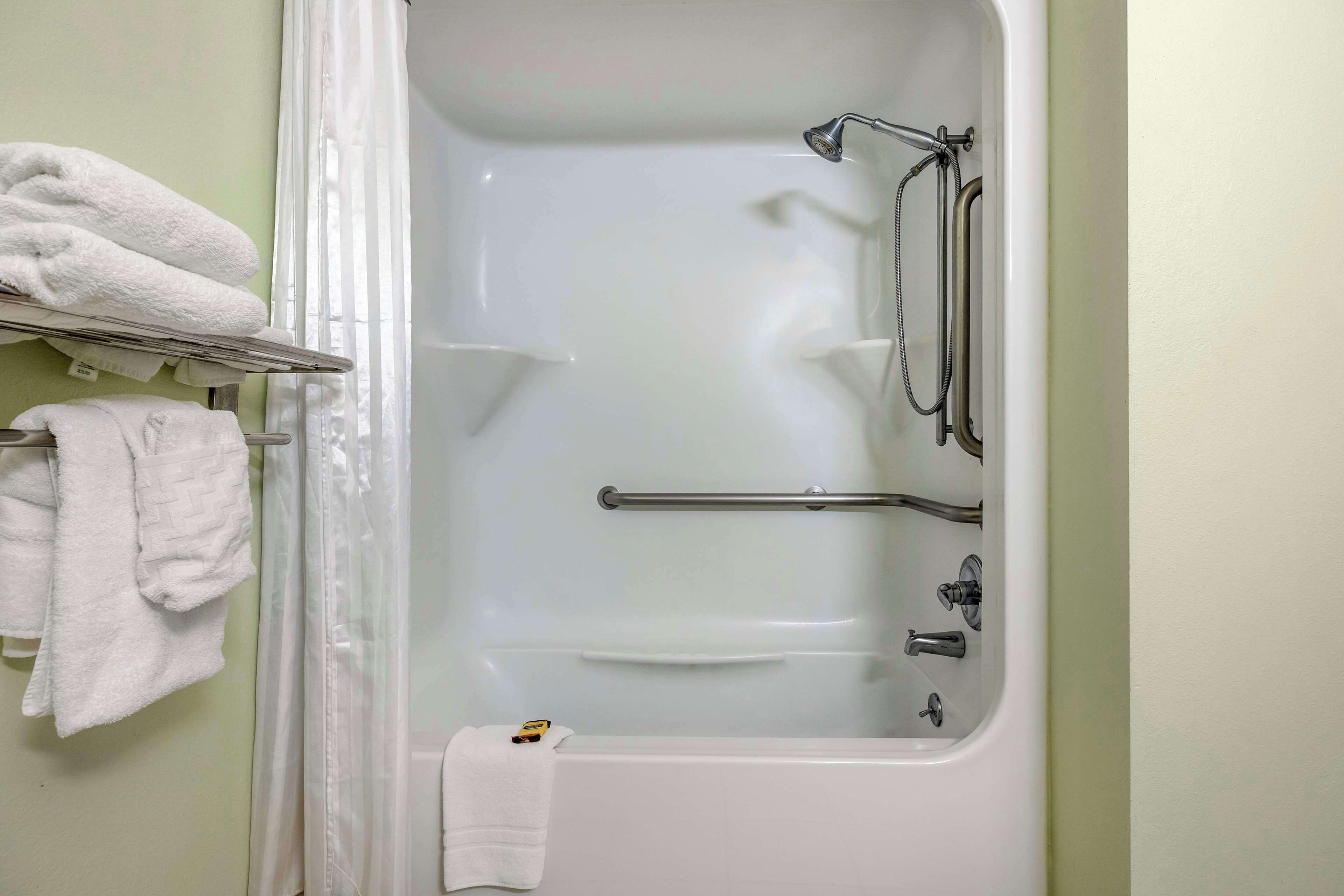A bathroom with a bathtub, grab bars, and a towel rack with towels.
