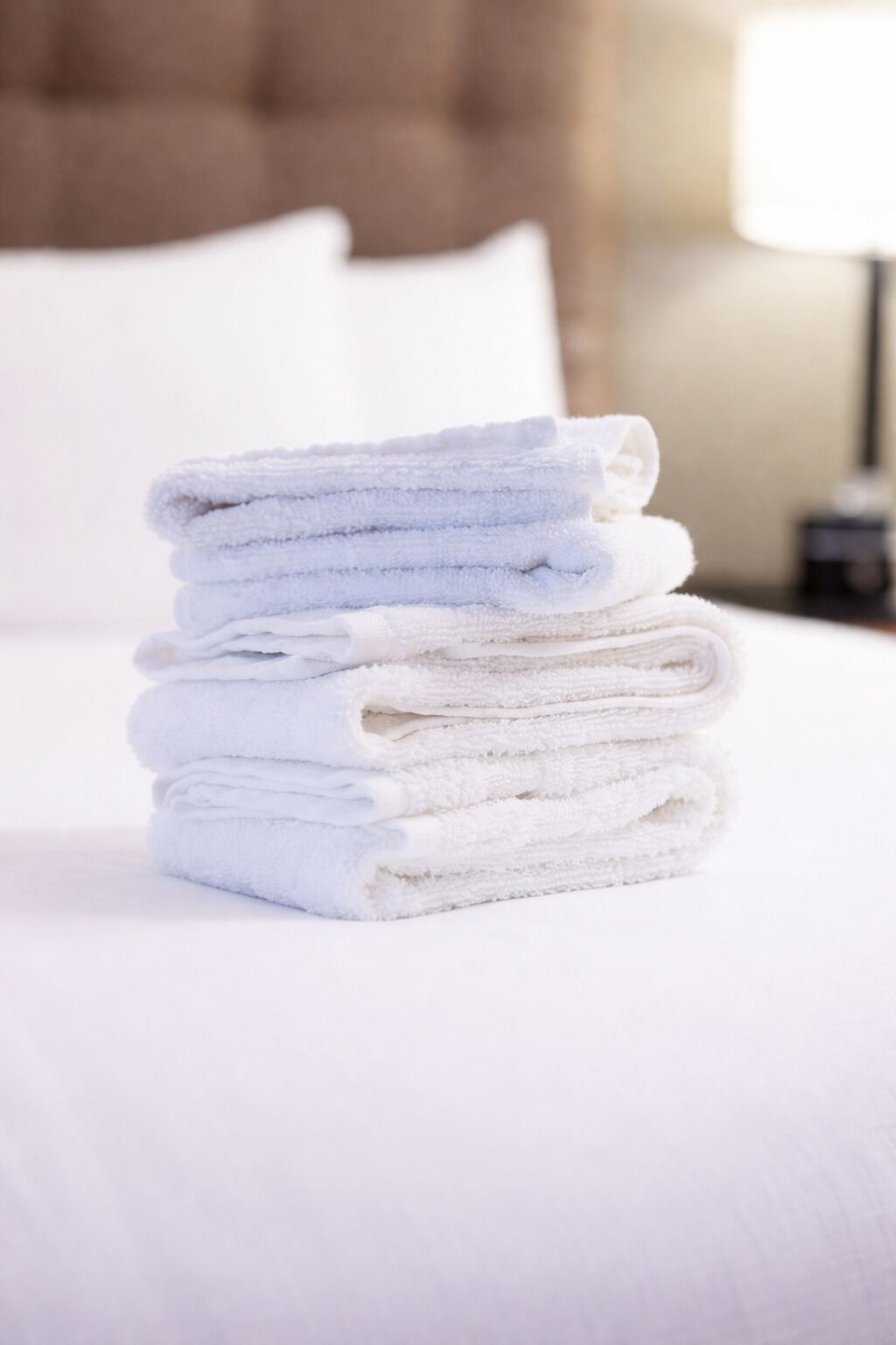 A stack of white towels on a bed with white sheets and a headboard.