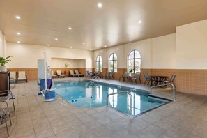 An indoor swimming pool with tiled flooring, lounge chairs, and tables.