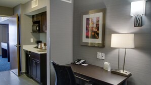 Een hotelkamer met een bureau, stoel, magnetron en een lijst met een abstract schilderij aan de muur.