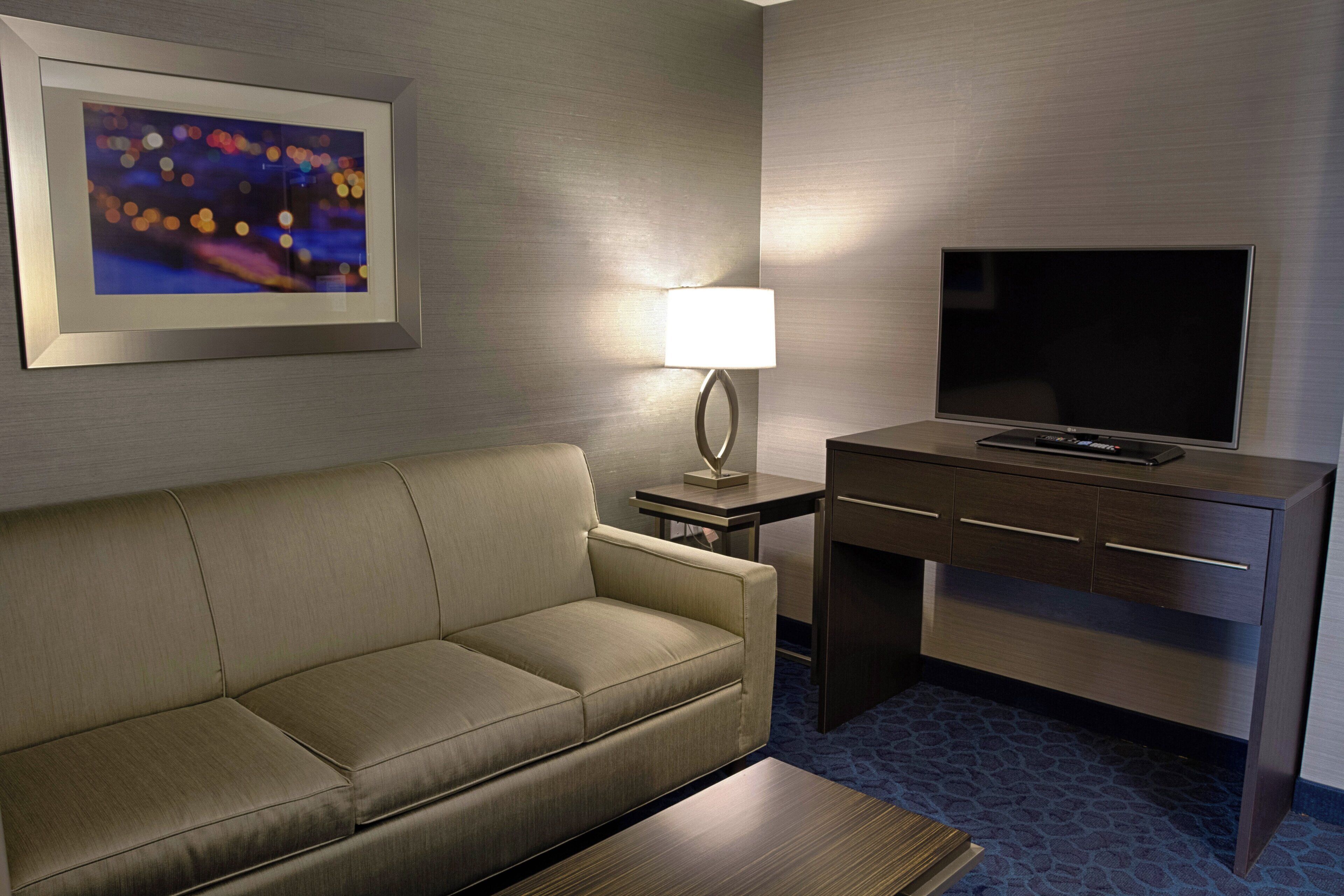 A hotel room with a sofa, a desk with a television, a lamp, and a framed picture on the wall.