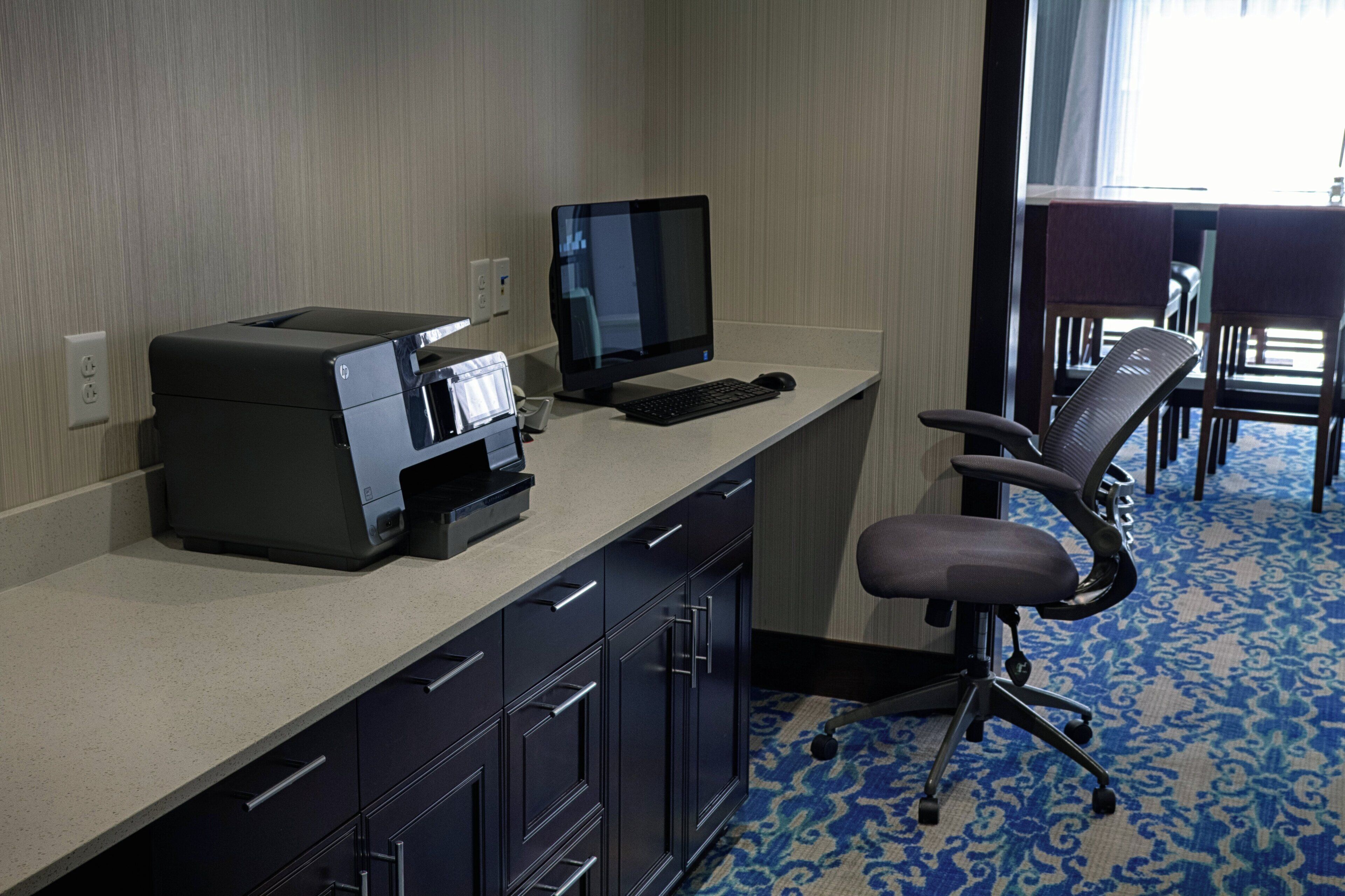 A hotel room with a desk, printer, computer, and office chair.
