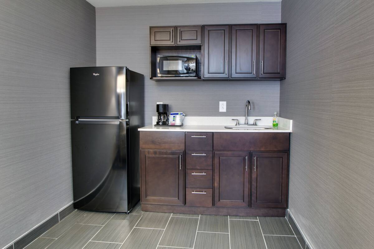A compact kitchen with dark wood cabinets, a stainless steel refrigerator, a microwave, and a coffee maker.