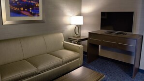 Een hotelkamer met een bank, een bureau met een flatscreen televisie, een lamp en een lijst met een afbeelding aan de muur.