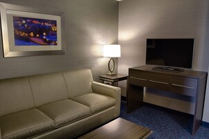 Habitación de hotel con sofá, escritorio, televisor de pantalla plana, lámpara y un cuadro en la pared.