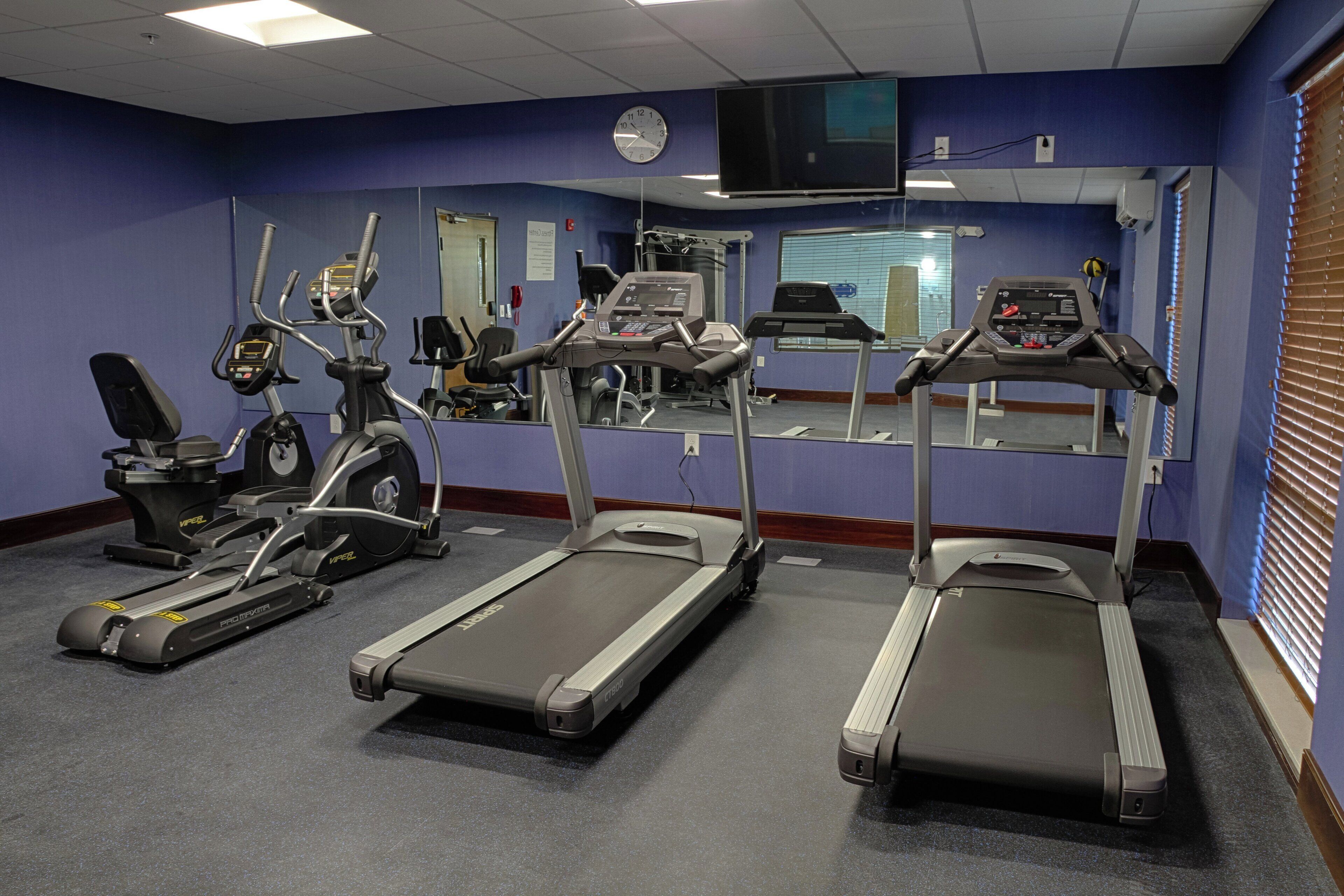 Une salle de sport équipée de tapis de course, d’appareils elliptiques et de vélos d’exercice.