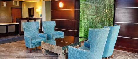 Un vestíbulo con mostrador de recepción, zona de estar con sillas y una mesa, y una pared verde con textura.