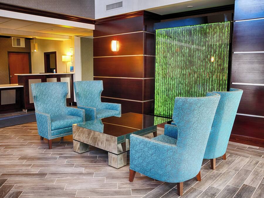 Un vestíbulo con mostrador de recepción, zona de estar con sillas y una mesa, y una pared verde con textura.