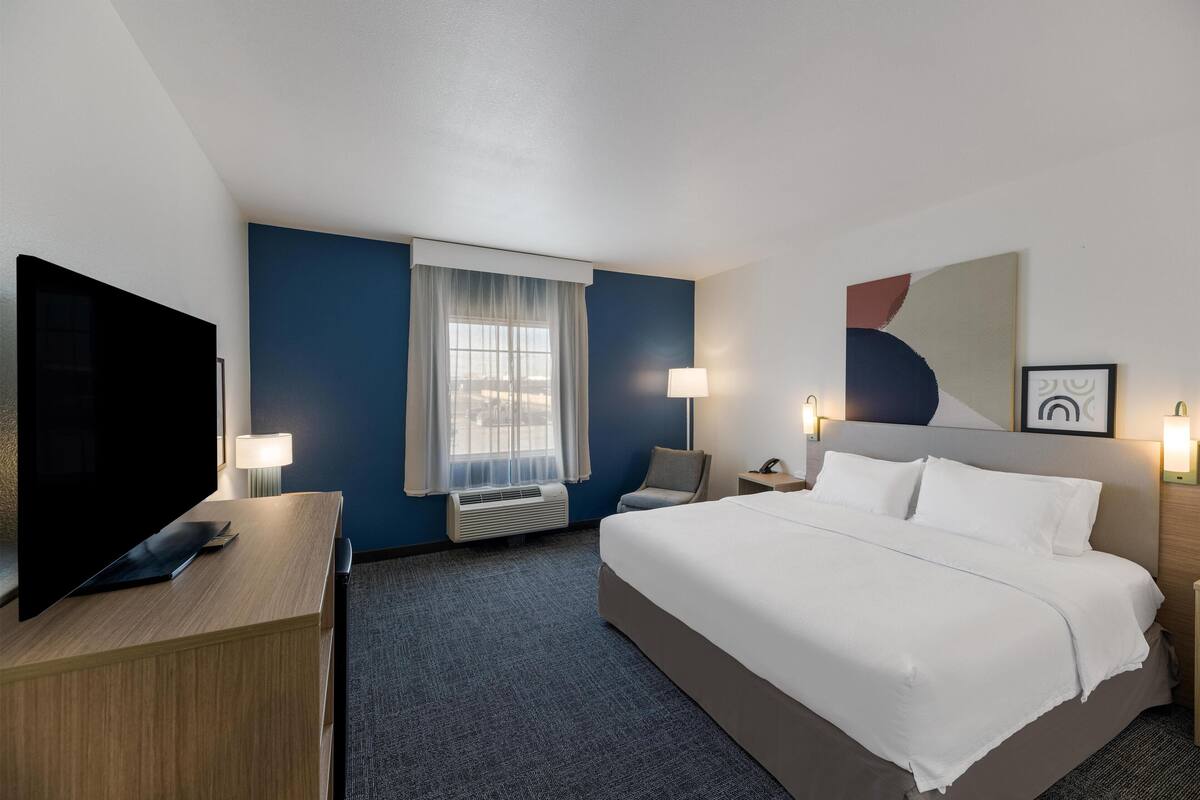 A hotel room with a large bed, a flat-screen TV, a desk, and a window with curtains.