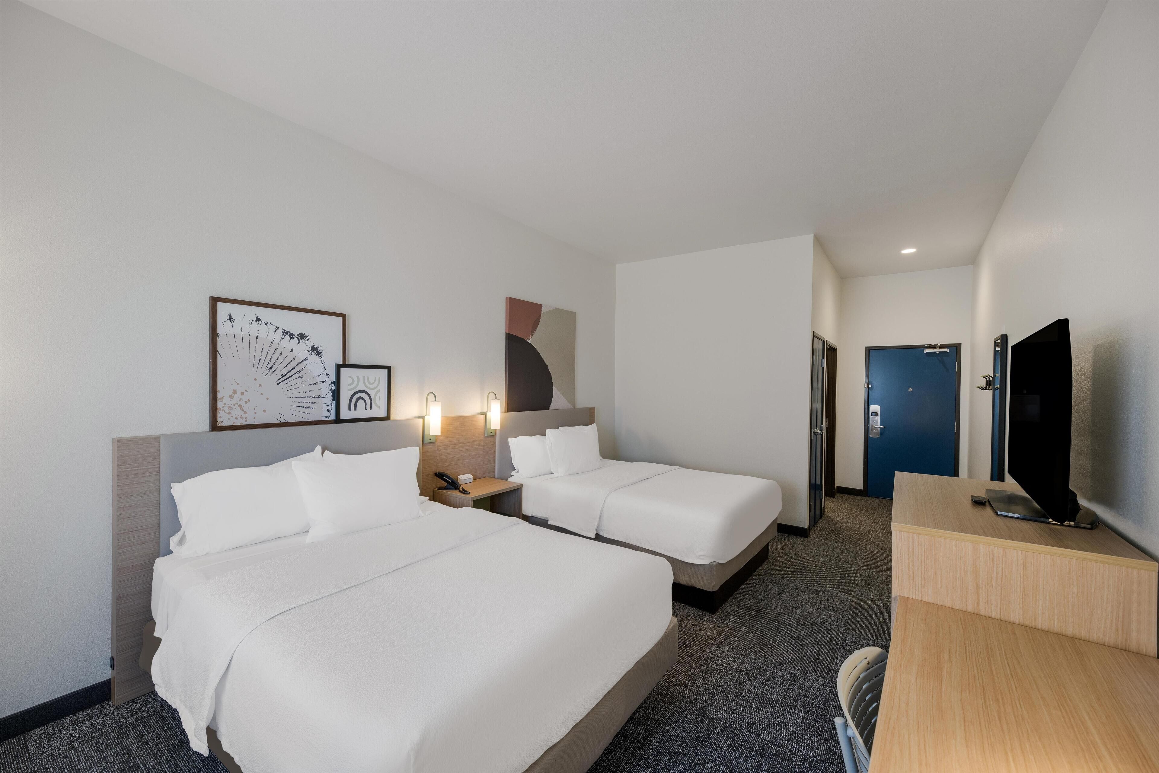 Een hotelkamer met twee bedden, een bureau, een televisie en kunstwerken aan de muren.