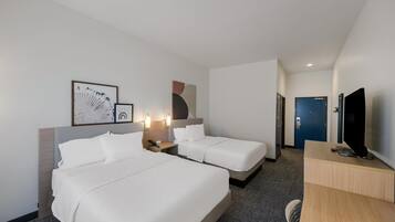 Une chambre d’hôtel avec deux lits, un bureau, une télévision et des œuvres d’art accrochées aux murs.