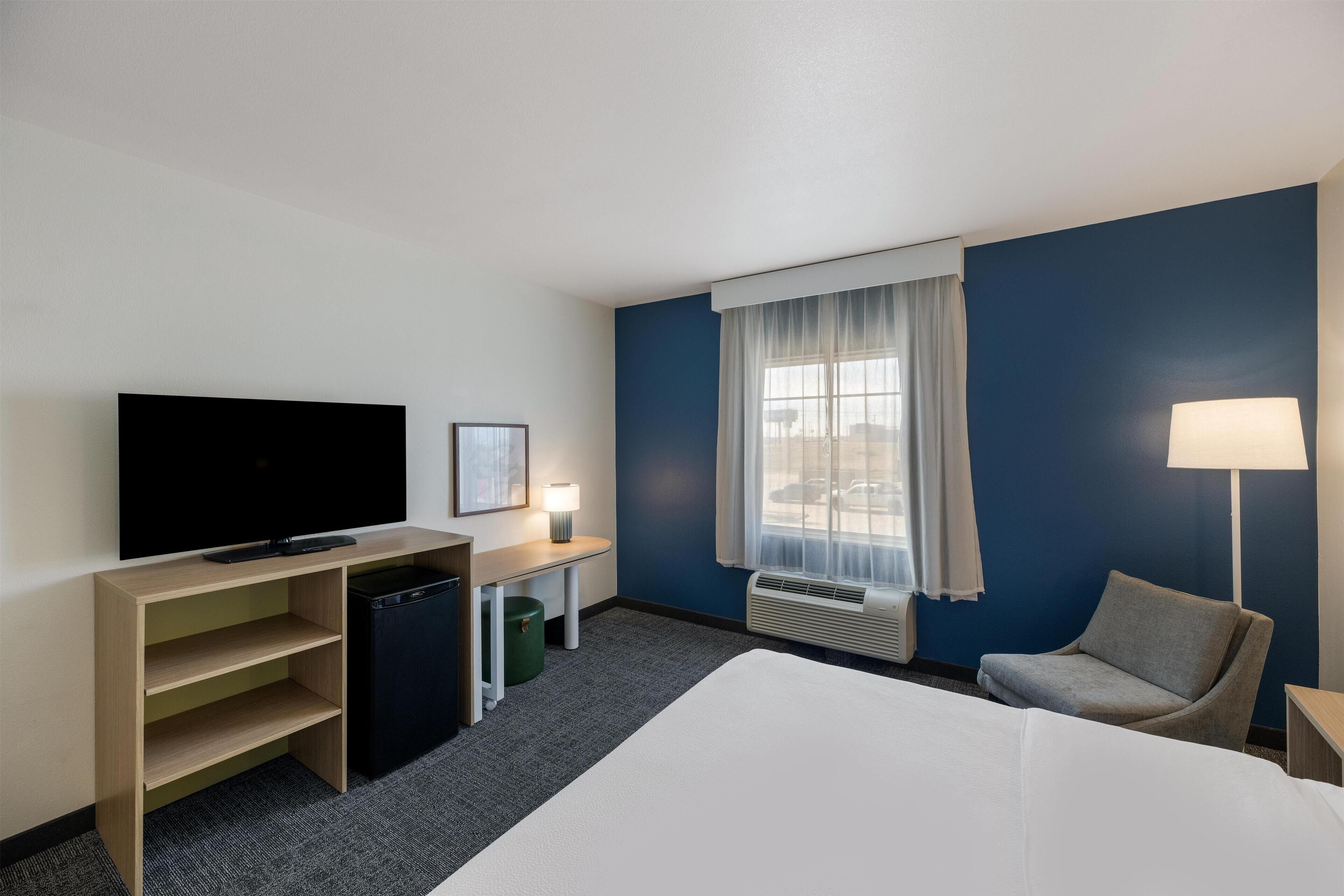 A hotel room with a bed, a desk, a television, a chair, and a window with curtains.
