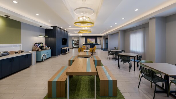 Una cucina moderna con isola centrale, una zona pranzo con tavoli e sedie in legno, e un soggiorno con divani e un tavolino.