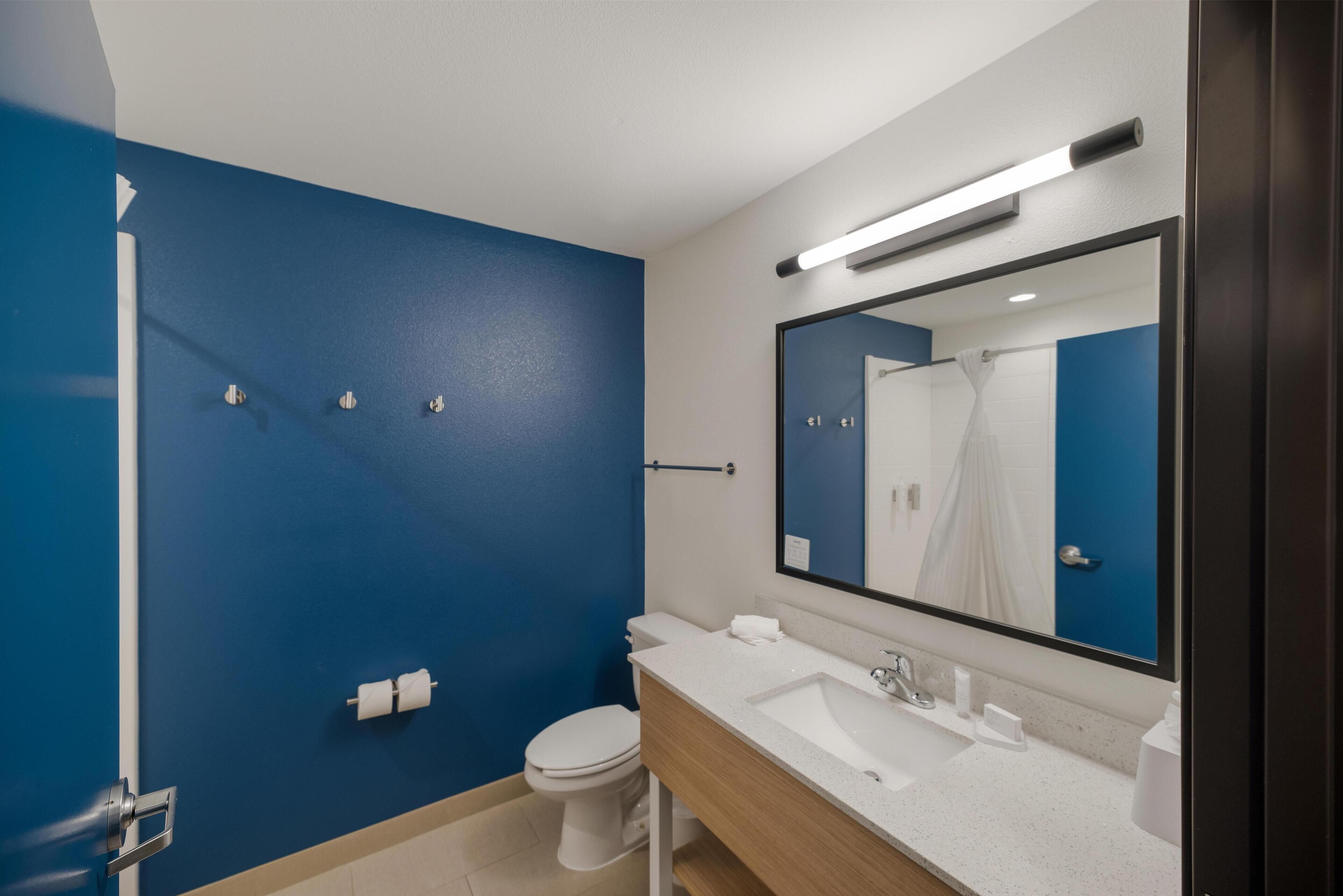 Ein modernes Badezimmer mit blauer Akzentwand, einer weißen Toilette, einem Waschbecken mit Spiegel und einer Duschkabine.