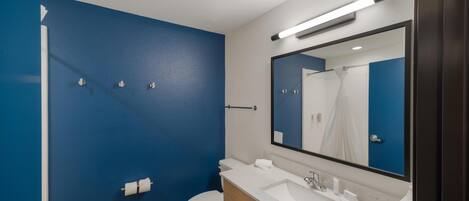 Ein modernes Badezimmer mit blauer Akzentwand, einer weißen Toilette, einem Waschbecken mit Spiegel und einer Duschkabine.