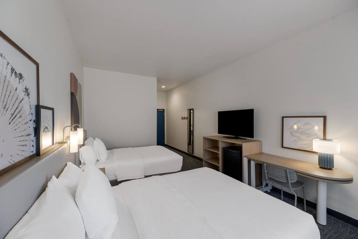 A hotel room with two beds, a desk, a television, and a lamp.