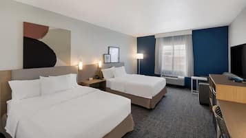 A hotel room with two beds, a desk, a chair, a lamp, and a large abstract painting on the wall.