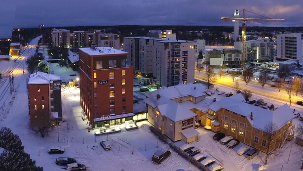 Un hotel de varios pisos, un estacionamiento cubierto de nieve y edificios circundantes.