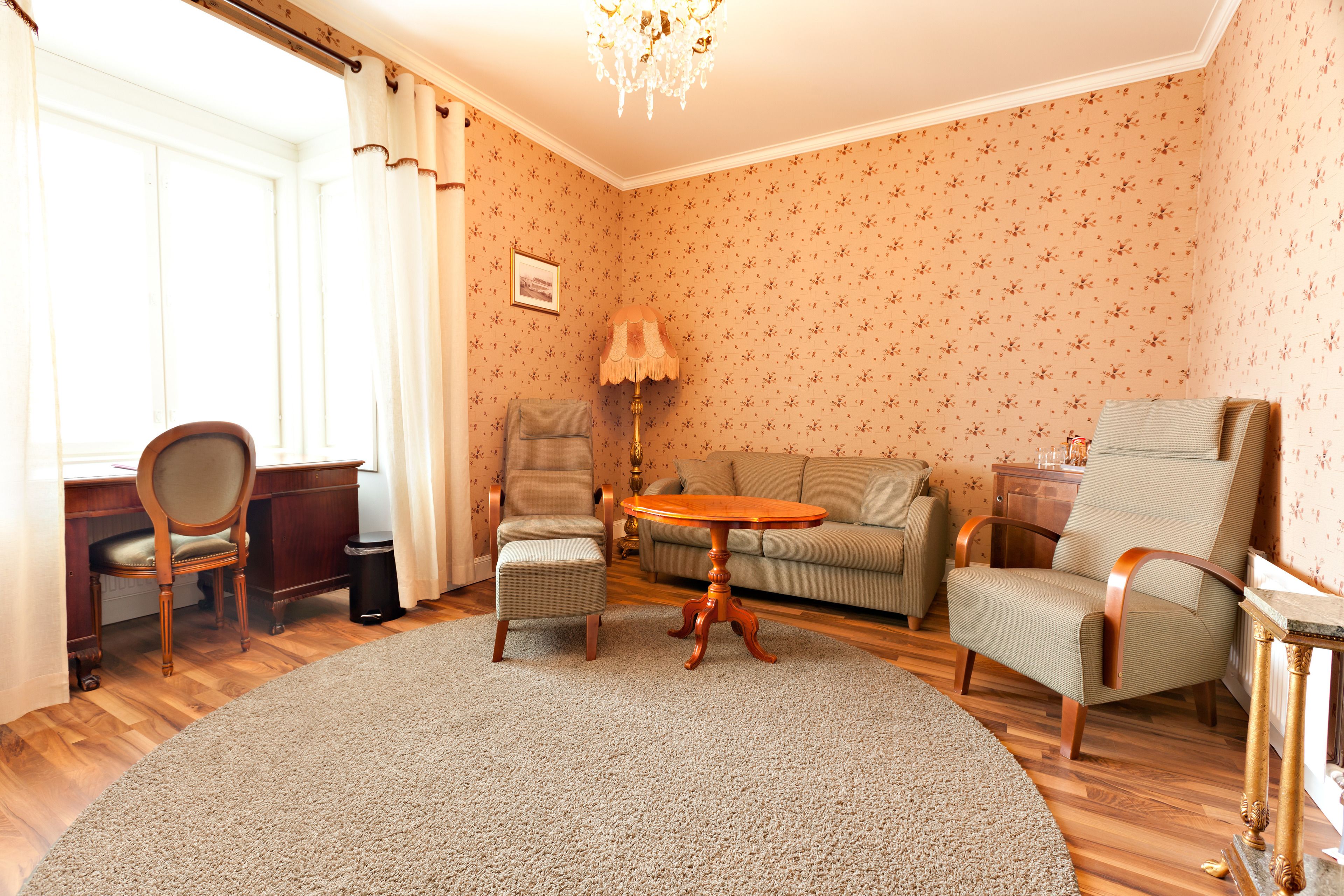A living room with a round wooden table, two armchairs, a sofa, a lamp, and a picture on the wall.